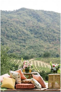 an outdoor seating area with pillows and vases on the table in front of a mountain