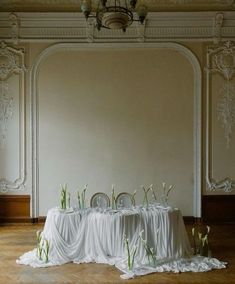 the table is covered with white cloths and flowers in front of an ornate wall