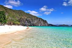 a beach with clear blue water and mountains in the background