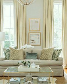 a living room filled with furniture and a chandelier hanging from the ceiling in front of two windows