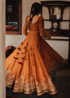 a woman standing in front of a mirror wearing an orange lehenga