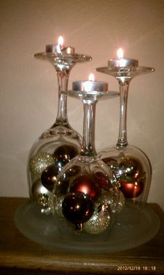 three wine glasses with candles in them sitting on a glass platter filled with ornaments