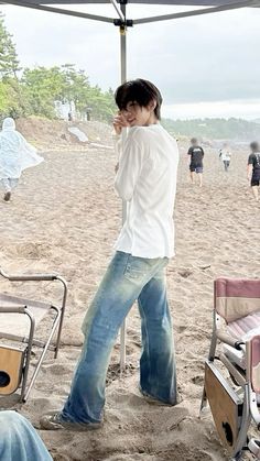 a man standing under an umbrella on the beach next to some chairs and a bench