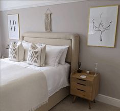 a bed with white linens and pillows in a bedroom next to two pictures on the wall