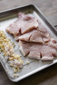 some meat is on a metal tray with seasoning and other food items next to it