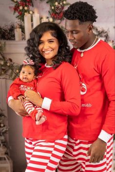 a man and woman in matching red pajamas holding a small child while standing next to a christmas tree