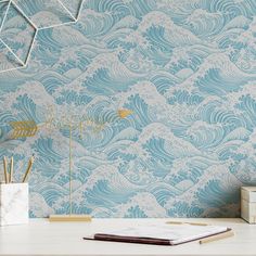 a desk with a book, pen and notebook on it next to a wallpapered background