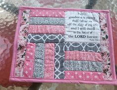 a pink and gray patchwork quilt with a bible verse written on the front in cursive writing