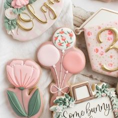 some decorated cookies are sitting on a white tablecloth with pink and gold decorations around them