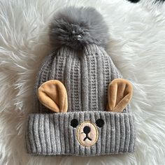 a knitted bear hat with ears on it sitting on top of a fluffy white blanket