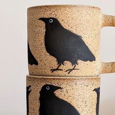 two mugs with black birds painted on them, one is sitting and the other is standing