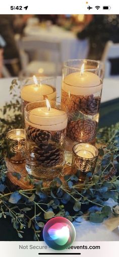 candles are sitting on a table with greenery and pine cones in the centerpiece