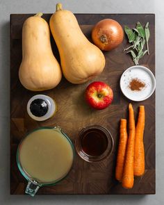 a cutting board topped with carrots, apples and other vegetables next to an apple cider