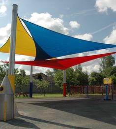 a large blue, yellow and red umbrella sitting on top of a parking lot next to a playground