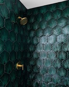 a green tiled bathroom with gold fixtures and palm leaves on the shower wall, along with a brass faucet