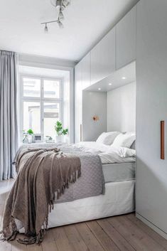 a bedroom with white walls and wood flooring has a large bed in the corner