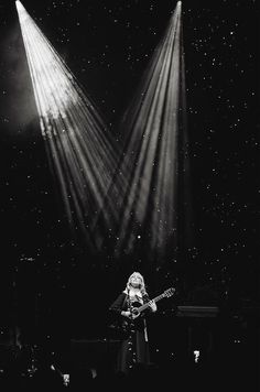 black and white photograph of a woman playing guitar on stage with three spotlights in the background