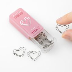 a person is holding some paper clips in front of a pink box with hearts on it