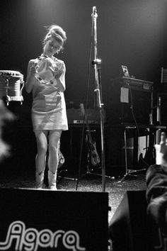 a woman standing in front of a microphone on stage next to another person sitting down