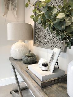 a wooden table topped with white vases next to a lamp and painting on the wall