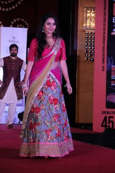 a woman in a pink and blue sari walking down the runway at an event