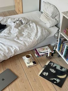 an unmade bed sitting on top of a wooden floor next to a book shelf