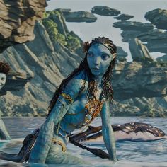 a woman with blue paint on her body sitting in front of some rocks and water