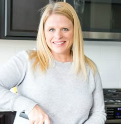 a woman standing in front of a stove holding a knife and cutting board with food on it