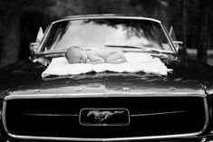 a baby laying on top of a blanket on the hood of a vintage mustang car