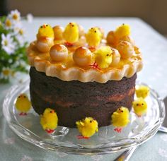 a chocolate cake topped with yellow chicks on top of a glass plate next to flowers