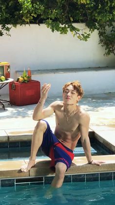 a young man sitting on the edge of a swimming pool with his legs up in the air