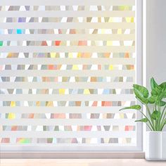 a potted plant sitting on top of a table next to a window covered in multicolored blinds