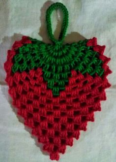 a crocheted strawberry ornament hanging on a white sheet with a green handle