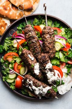 a plate filled with meat and veggies on skewers next to pita bread