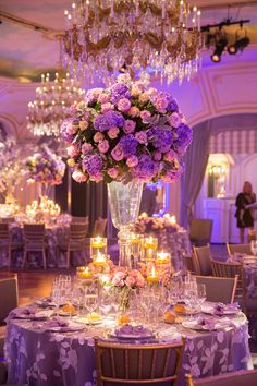 an elegant table setting with purple flowers and candles in the center, surrounded by chandeliers