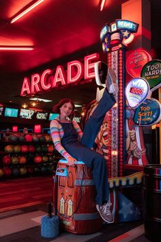 a woman sitting on top of a barrel in front of a neon sign that reads arcade