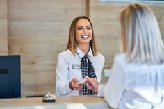 a woman in a white shirt and tie is talking to another woman who is sitting at a desk