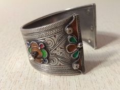 This is a Beautiful silver berber bracelet from the Anti Atlas region in Morocco. The decoration is very refined, there's some remains of black deco and enamel in yellow and green. This bracelet shows an exquisite quality of engraved work with flower motifs. The center stone is an glass in red color. Min Width : 2,5 cm (0,98 inches) Max Width : 4,2 cm (1,6 inches) Inner diameter : 5,8 cm (2,3 inches) Weight : 56,7 g Bohemian Silver Bracelets With Meenakari, Silver Bohemian Bracelets With Inlay, Traditional Inlay Bracelets Perfect For Gifts, Traditional Inlay Bracelets As Gift, Traditional Inlay Cuff Bangle Bracelet, Traditional Silver Bangle With Meenakari, Traditional Adjustable Inlay Bracelets, Traditional Adjustable Inlay Cuff Bracelet, Traditional Adjustable Cuff Bracelet With Inlay