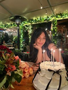 a woman sitting in front of a white cake with lit candles on top of it