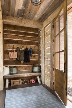 a wooden room with a bench, rug and coat rack on the wall next to an open door