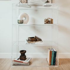 a clear shelf with books and other items on it in front of a white wall