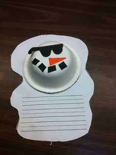 a paper plate with a snowman face on it sitting on top of a wooden table