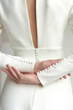 the back of a woman's white dress with pearls on her arms and hands