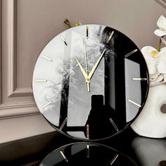 a black and white clock sitting on top of a table next to a vase with flowers