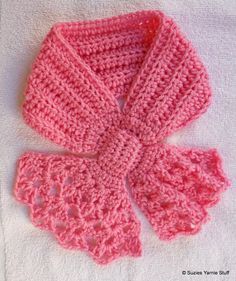 a pink crocheted scarf and booties on a white towel in the shape of a bow