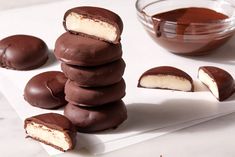 a stack of chocolate covered donuts sitting on top of a white napkin next to a bowl of chocolate