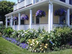 a white house with purple and yellow flowers in the front yard