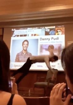 a woman taking a photo of a man in front of a projector screen with his legs spread out