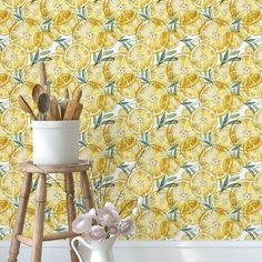 a white vase filled with lemons next to a yellow wallpapered background and wooden stool