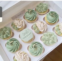 twelve cupcakes with green and white frosting in a cardboard box on top of a table